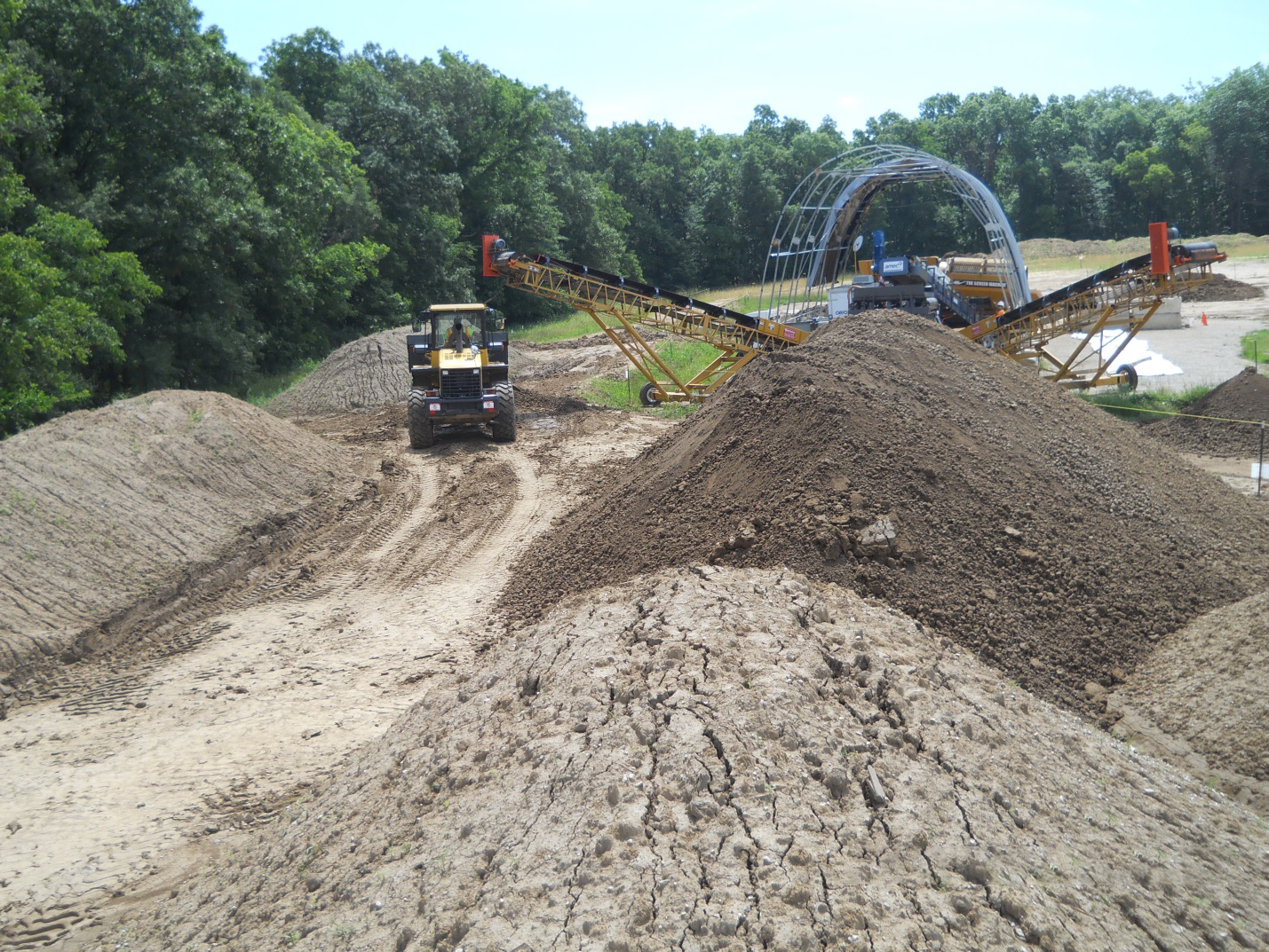 Photo at Iowa Army Ammunition Plant of environmental remediation work with piles of dirt, construction equipment, and the frame of an arched building in the background