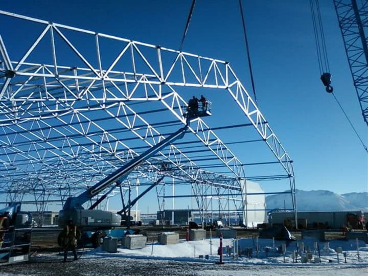 Photo of white building frame being assembled with blue sky seen in the background